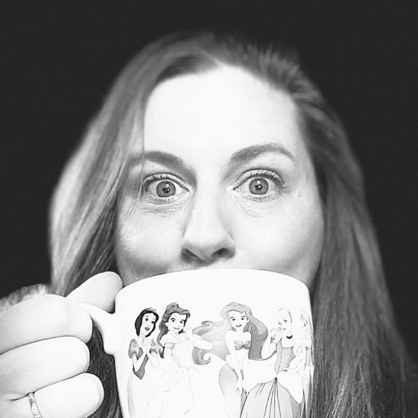 Woman holding a Disney princess-themed mug, looking surprised.