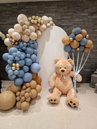 Baby shower balloon display. Teddy bear sat on the floor holding balloons up in blue and brown. 