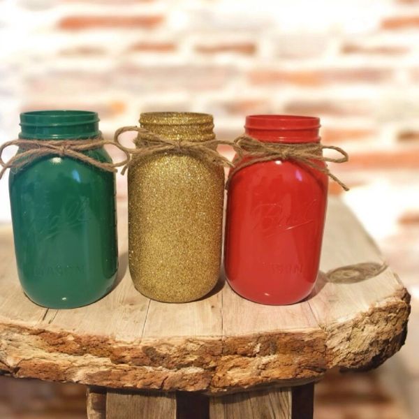Three decorated mason jars in green, gold glitter, and red with twine bows.