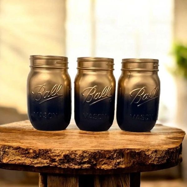 Three gradient-painted Ball Mason jars on a rustic wooden surface.