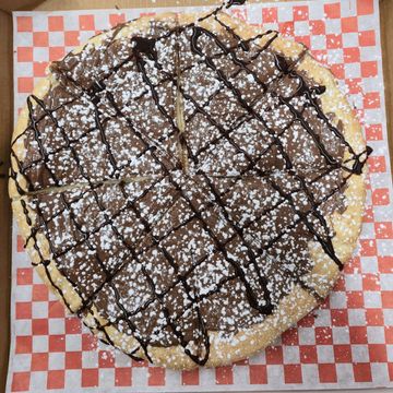 Neutella spread on perfectly baked pizza dough, garnish with icing sugar and chocolate drizzle.