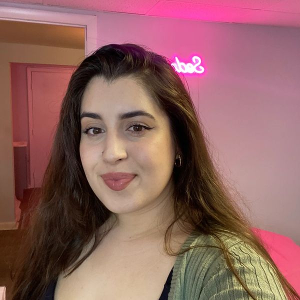 A woman with long hair smiling in a room with pink lighting.