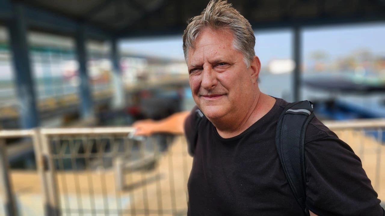 Middle-aged man with a backpack at a waterfront location.
