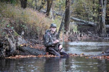 Person fishing in a river wearing camouflage.