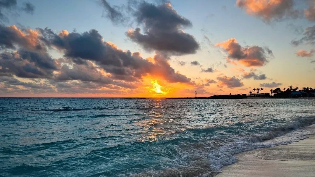 Sunset over a calm ocean with scattered clouds and a distant shoreline.