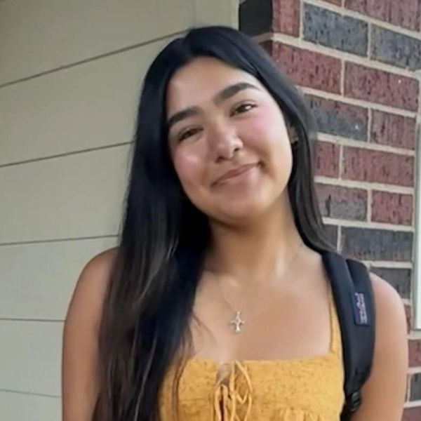 Young woman smiling wearing yellow top and backpack.