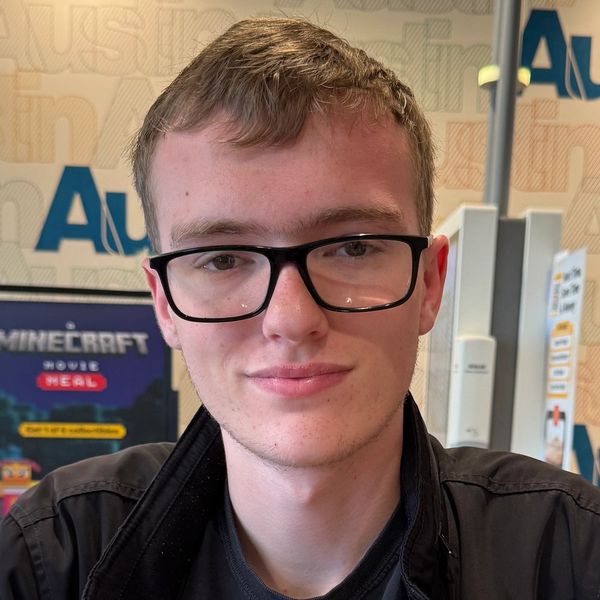 Young man with glasses smiling indoors.