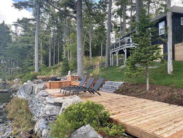 Wooden deck with lounge chairs by a lakeside cabin surrounded by trees.