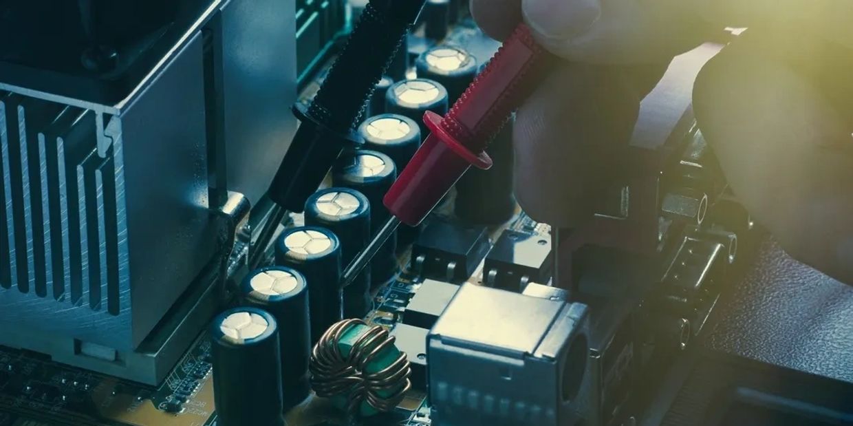 Technician testing electronic components on a circuit board with probes.