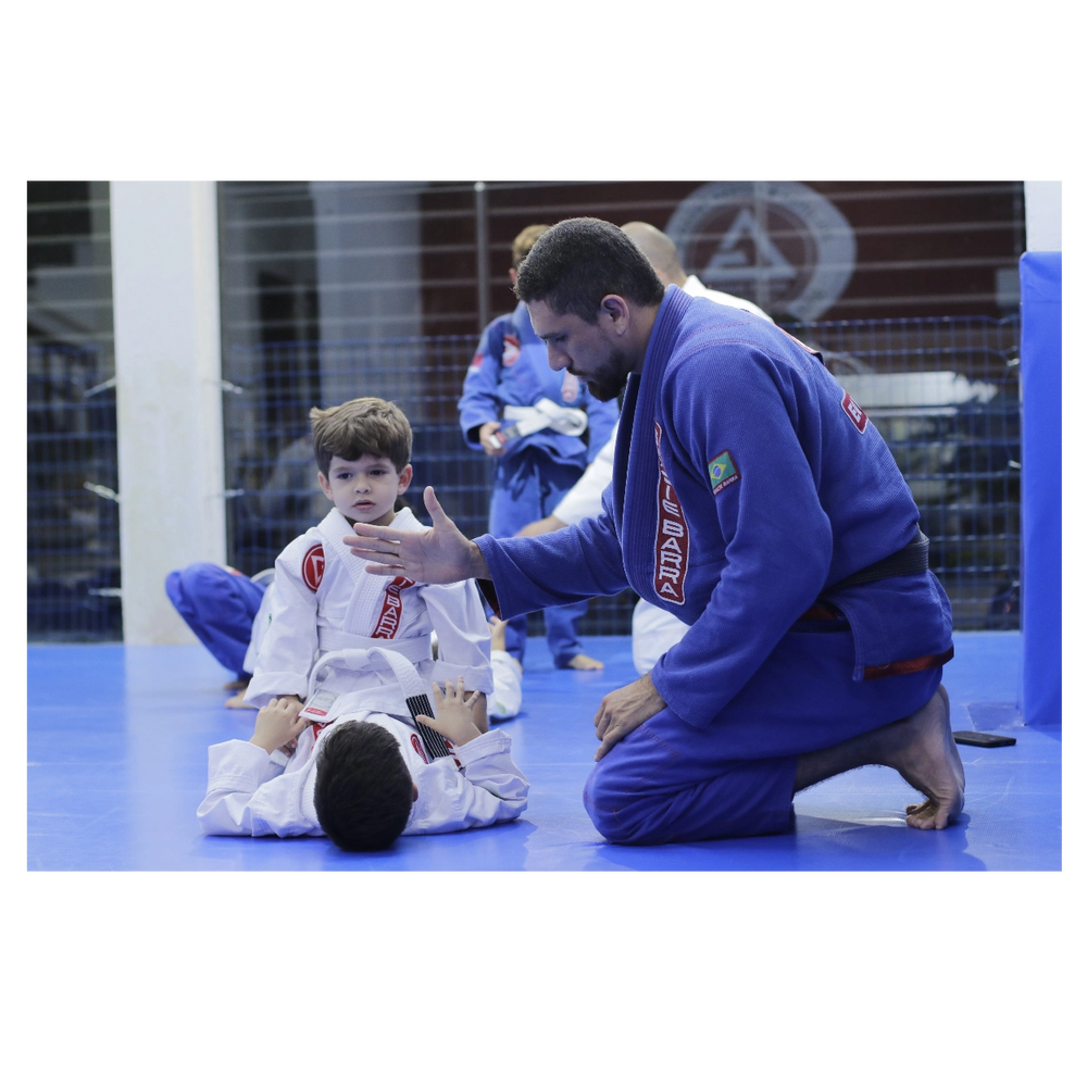 Criança treinando Jiu-Jitsu e Defesa Pessoal e um Professor Faixa Preta supervisionando.