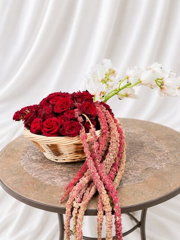 Basket of red roses and trailing flowers on a round table.