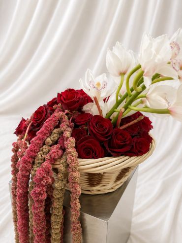 Basket of red roses and white orchids with hanging flowers.
