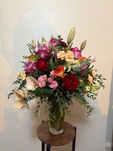 Elegant mixed flower bouquet in a glass vase on a wooden stool.
