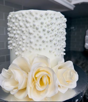 Elegant white cake adorned with pearls and cream roses.
