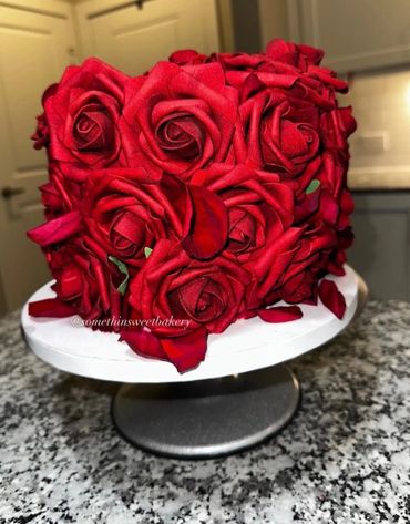 Cake decorated with realistic red rose petals on a white stand.