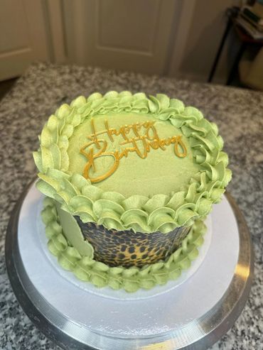 Green birthday cake with leopard print and gold "Happy Birthday" topper.