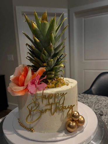 Elegant birthday cake with pineapple top and golden decorations.