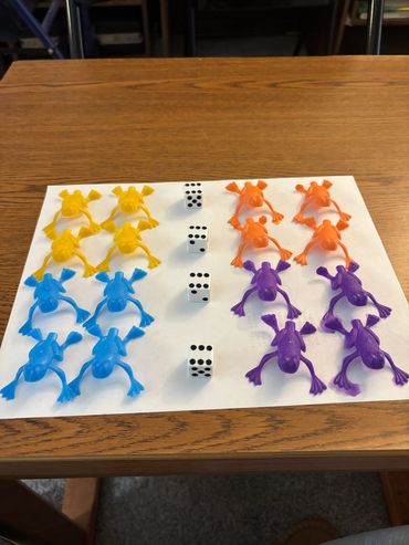 Colorful plastic frogs and dice on a paper.