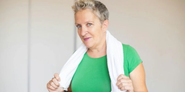 Woman with short hair in green shirt holding a white towel after workout.