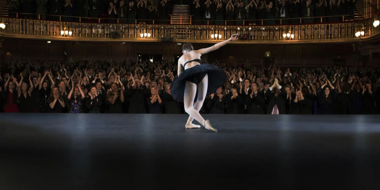 Ballet dancer takes a bow on stage to applause.