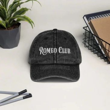 Black cap with 'ROMEO CLUB' text on a white table.
