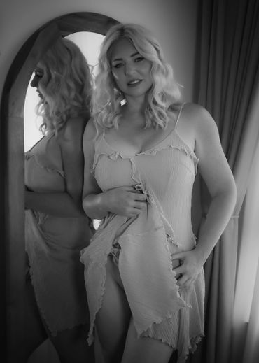 Black and white portrait of a woman in a delicate dress by a mirror.