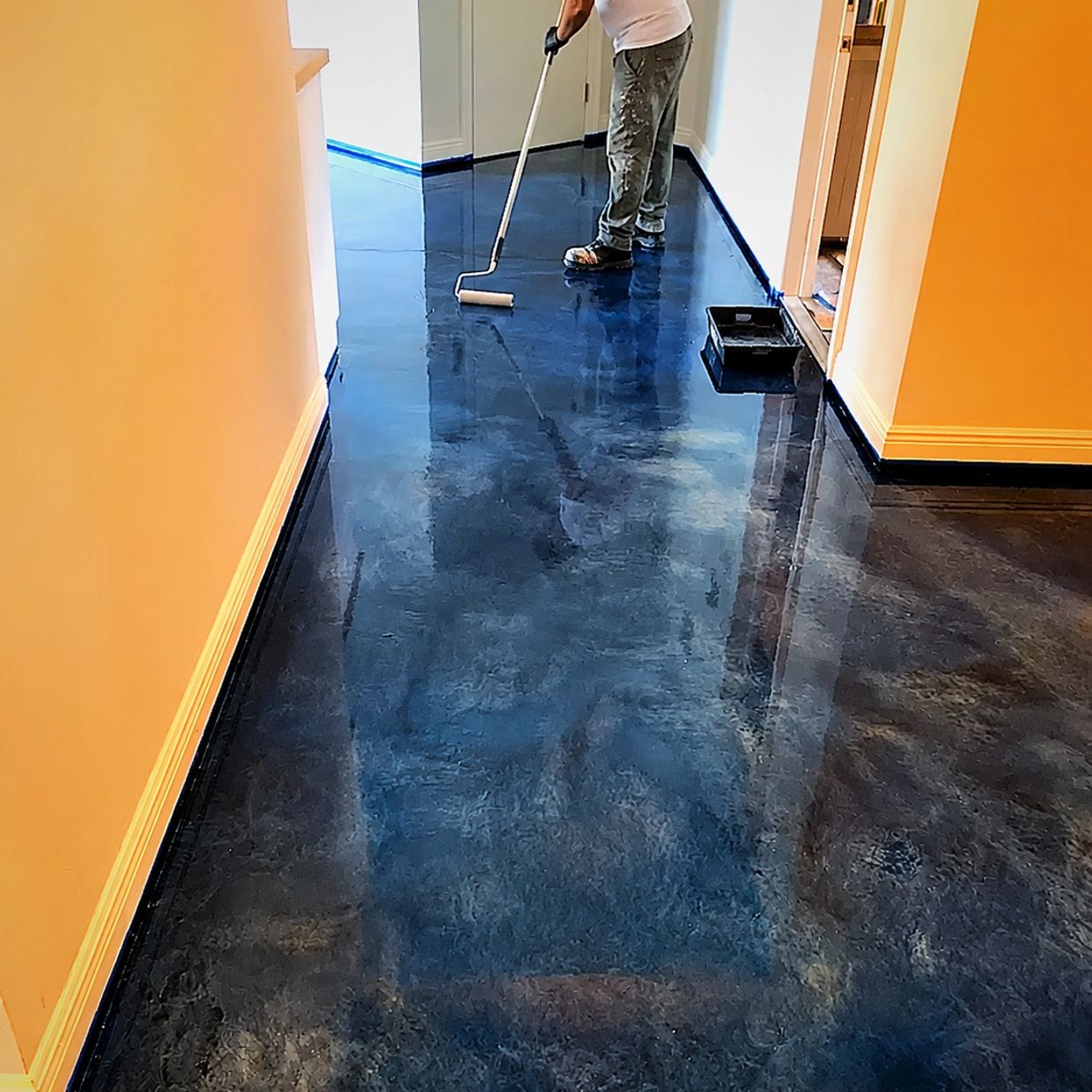 Person applying epoxy floor coating in hallway.