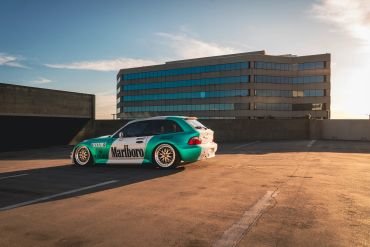 A green and white Marlboro-themed race car parked on a rooftop at sunset.