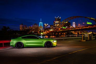 A green sports car parked at night with a city skyline and bridge in the background.