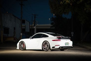 White Porsche sports car parked on a dimly lit urban street at night.