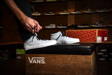 Person tying white Vans sneakers in a skate shop.