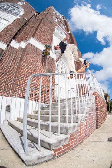 Skateboarder performing a trick on a handrail by a brick building.