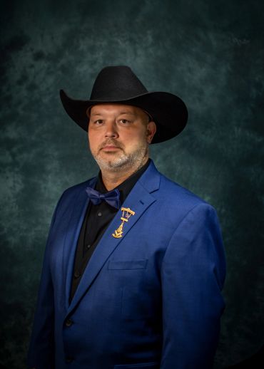 Man in a blue suit and black cowboy hat posing for a portrait.