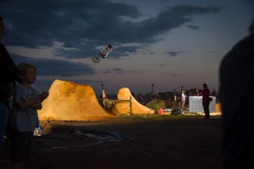 BMX rider performs a high jump at dusk with spectators watching.