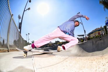 Skateboarder performing a stylish slide trick in a sunny skatepark.