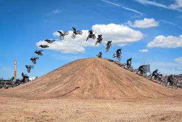 Sequence of a motocross rider jumping over a dirt mound under a blue sky.