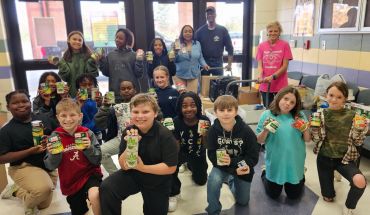 A group of children proudly holding various canned goods indoors.