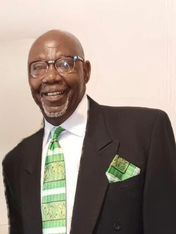 Smiling man in a black suit with a green patterned tie and matching pocket square.