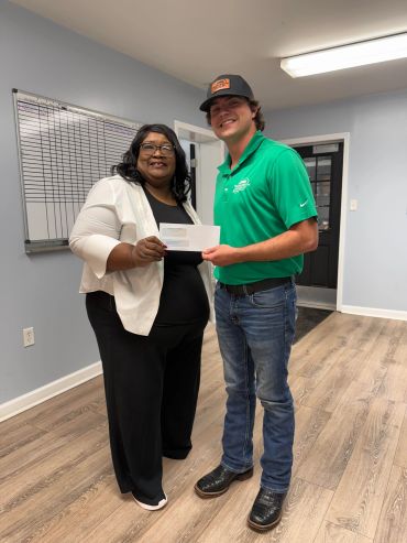 Two people smiling and holding a check indoors.