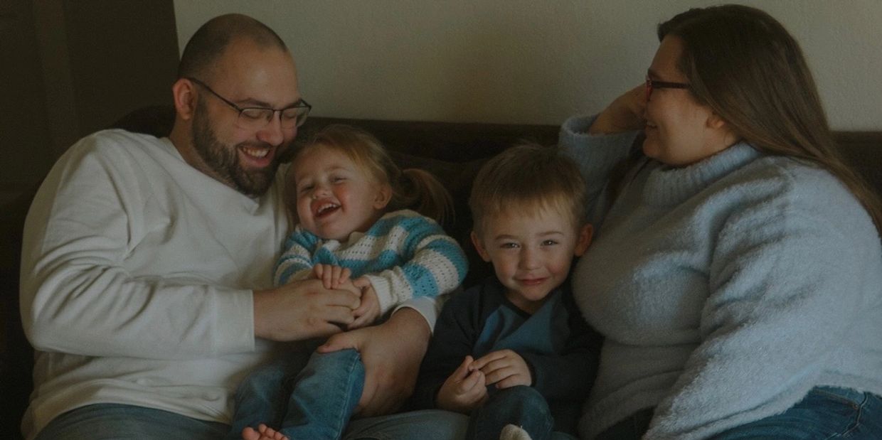 A happy family of four laughing together on a couch.