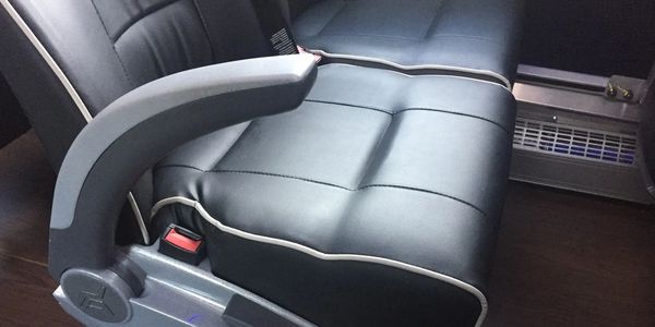 Close-up of a black leather seat with armrest and seatbelt buckle.