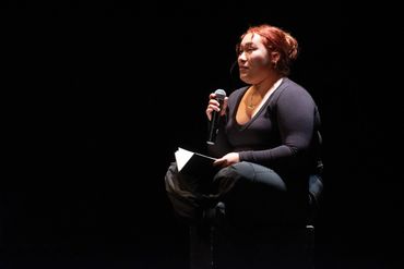 Mairin Mendoza sitting cross-legged performing a monologue on love.
