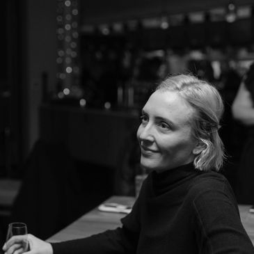 A woman smiling thoughtfully in a dimly lit setting.