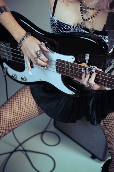 Person playing electric bass guitar with edgy fashion and accessories.