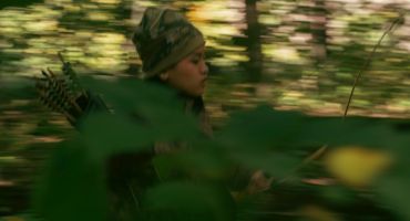 Person in camouflage gear moving swiftly through dense forest foliage.
