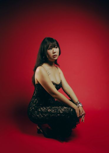 Woman in a black lace dress posing against a red background.