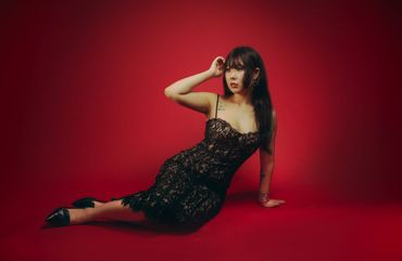 Woman in a black lace dress poses against a red background.
