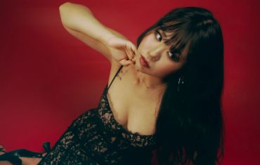 A woman with long dark hair poses against a red background.