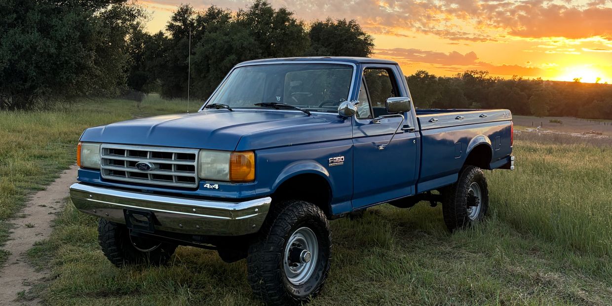 A blue Ford F-350 4x4 pickup truck parked on grass at sunset.
