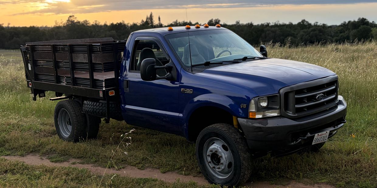 Blue Ford F-450 flatbed truck parked in a grassy field at sunset.